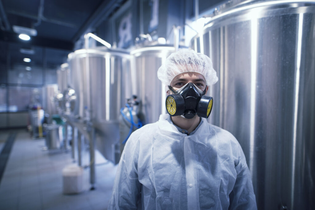Man in white protective uniform with hairnet and protective mask handling hazardous chemicals.